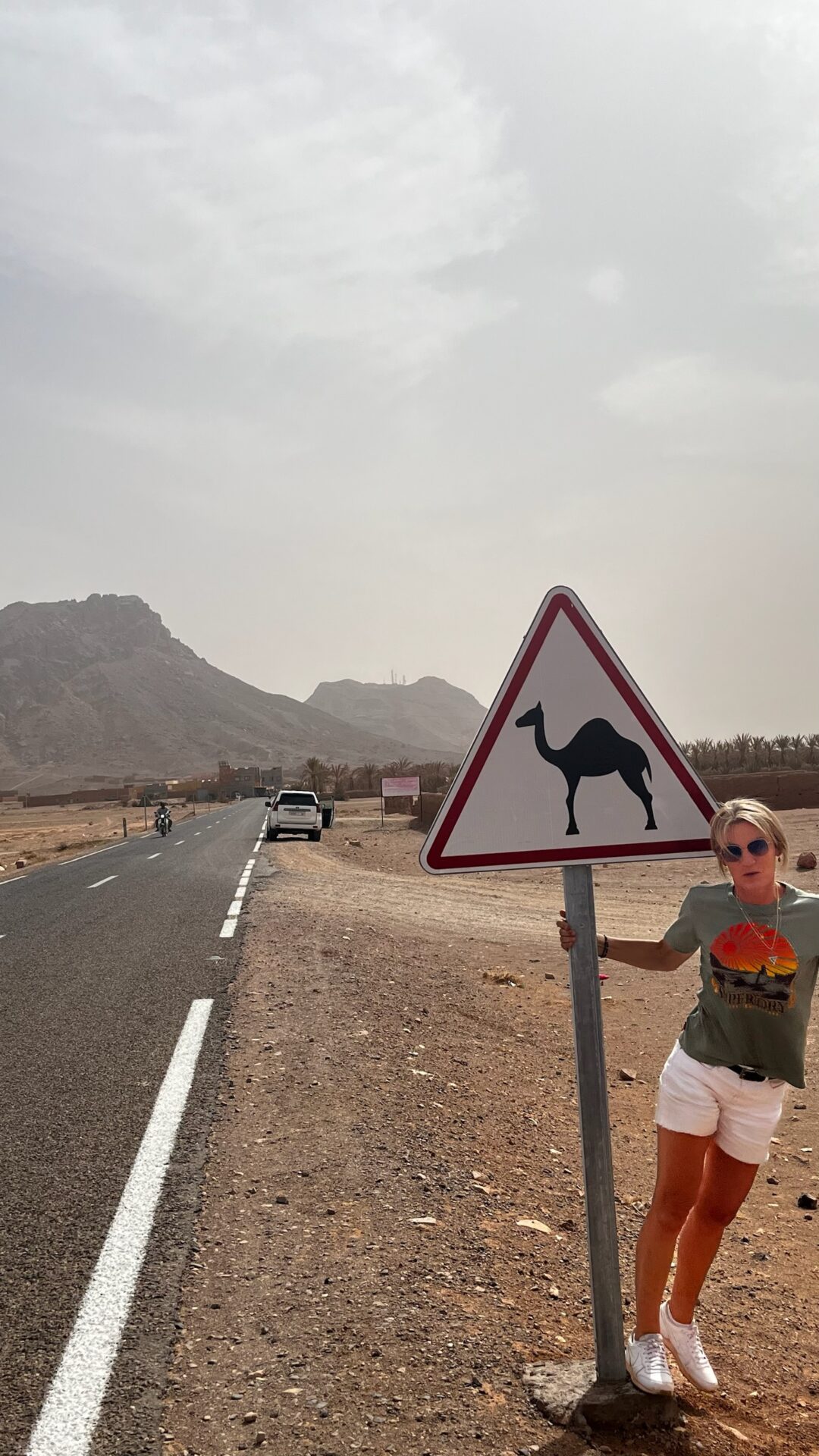 Voyageuse posant près d'un panneau « attention dromadaires »