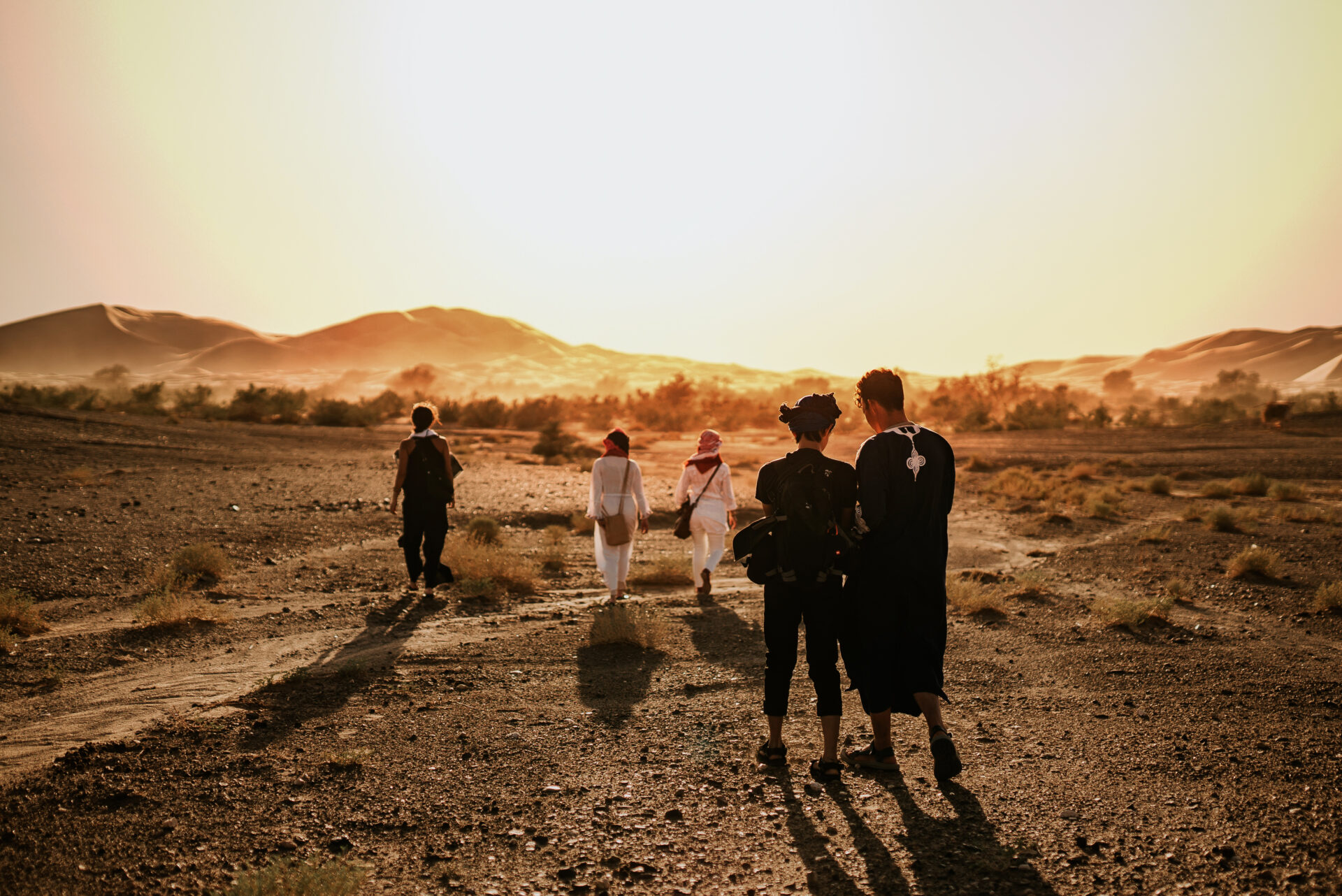 Petit groupe de voyageurs marchant vers les dunes au coucher du soleil